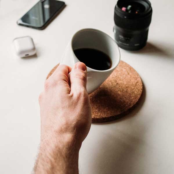 Close up of a man's hand holding a white mug of black coffee.